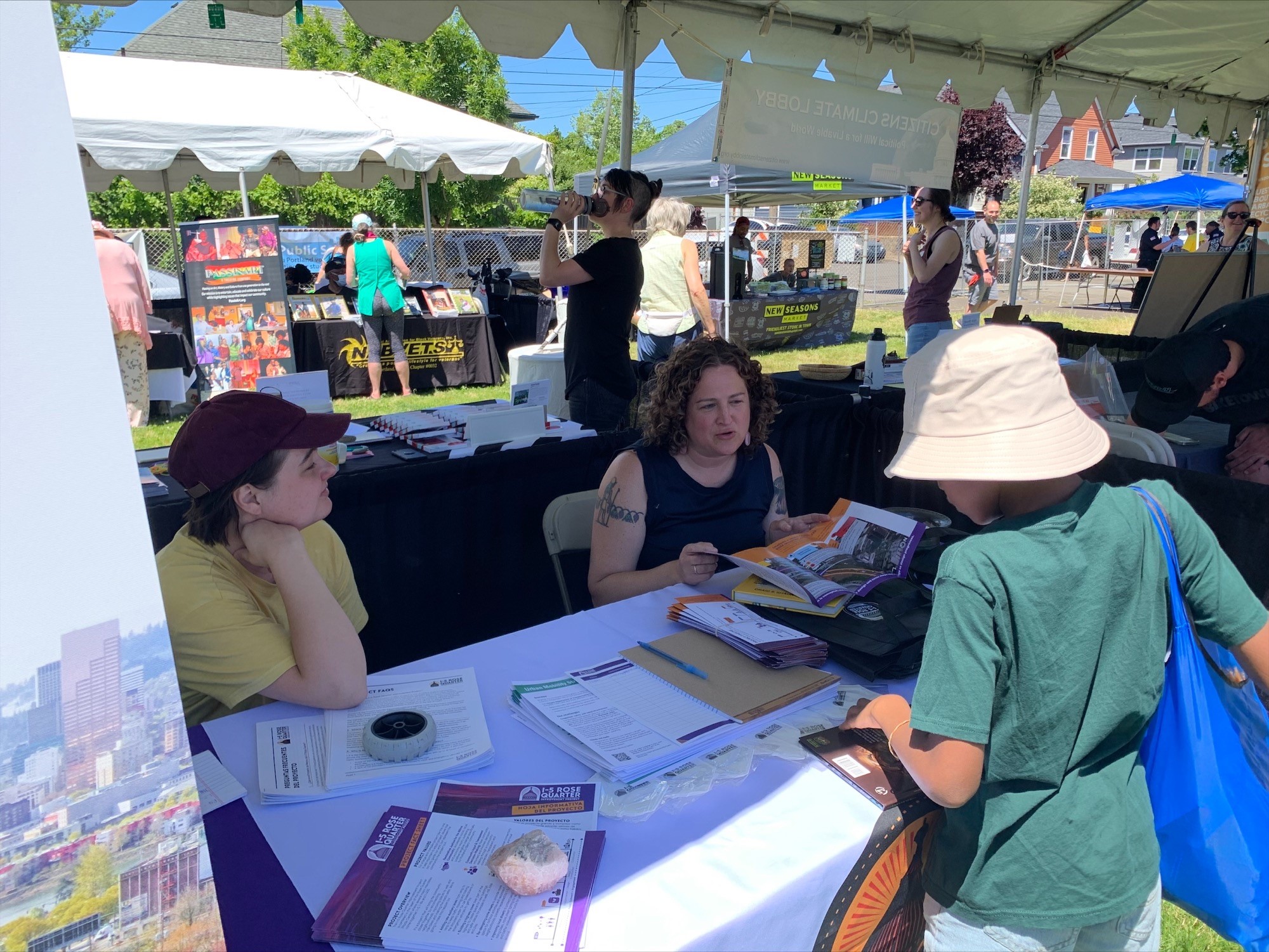 Two staff members sitting behind a table, pointing to materials on the table while in a discussion with a festival attendee.