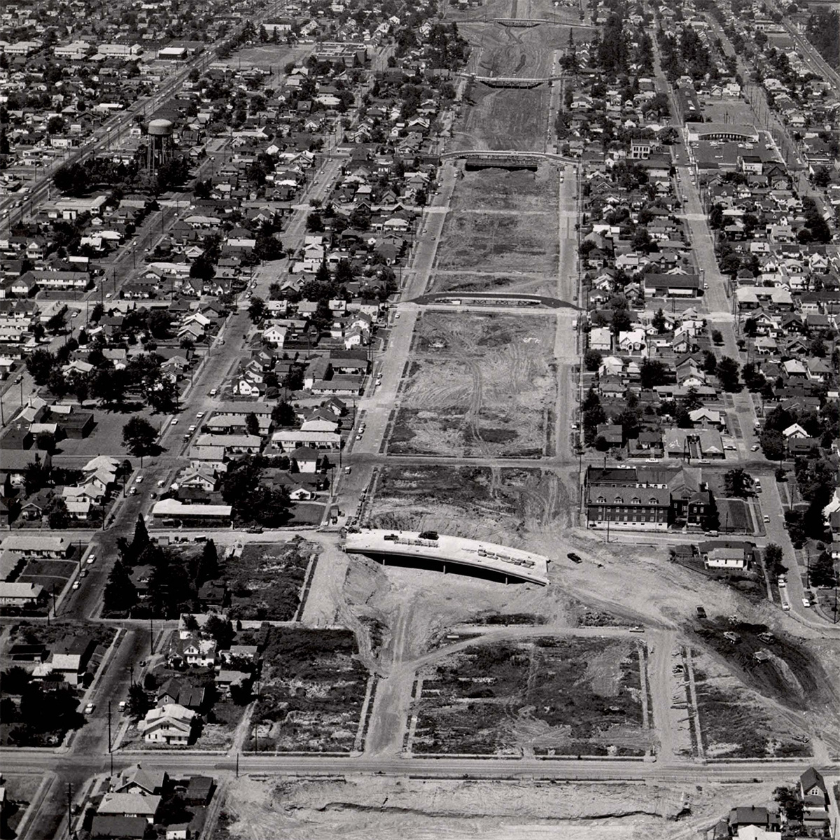 Black and white aerial photograph from N Minnesota Avenue looking north. The neighborhood lots that have been cleared to allow for construction of I-5 appear as a scar on the landscape.